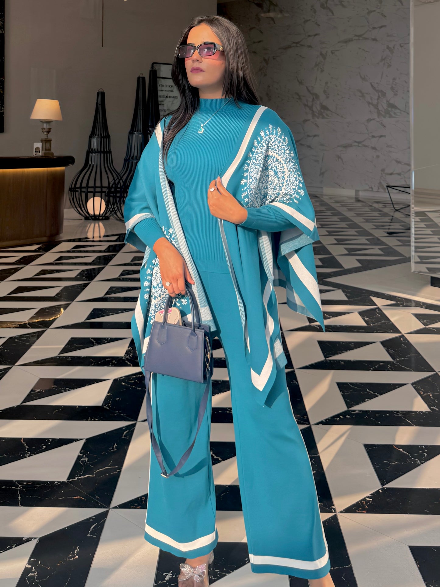 Woman in a blue outfit with white patterns standing on a black and white patterned floor.